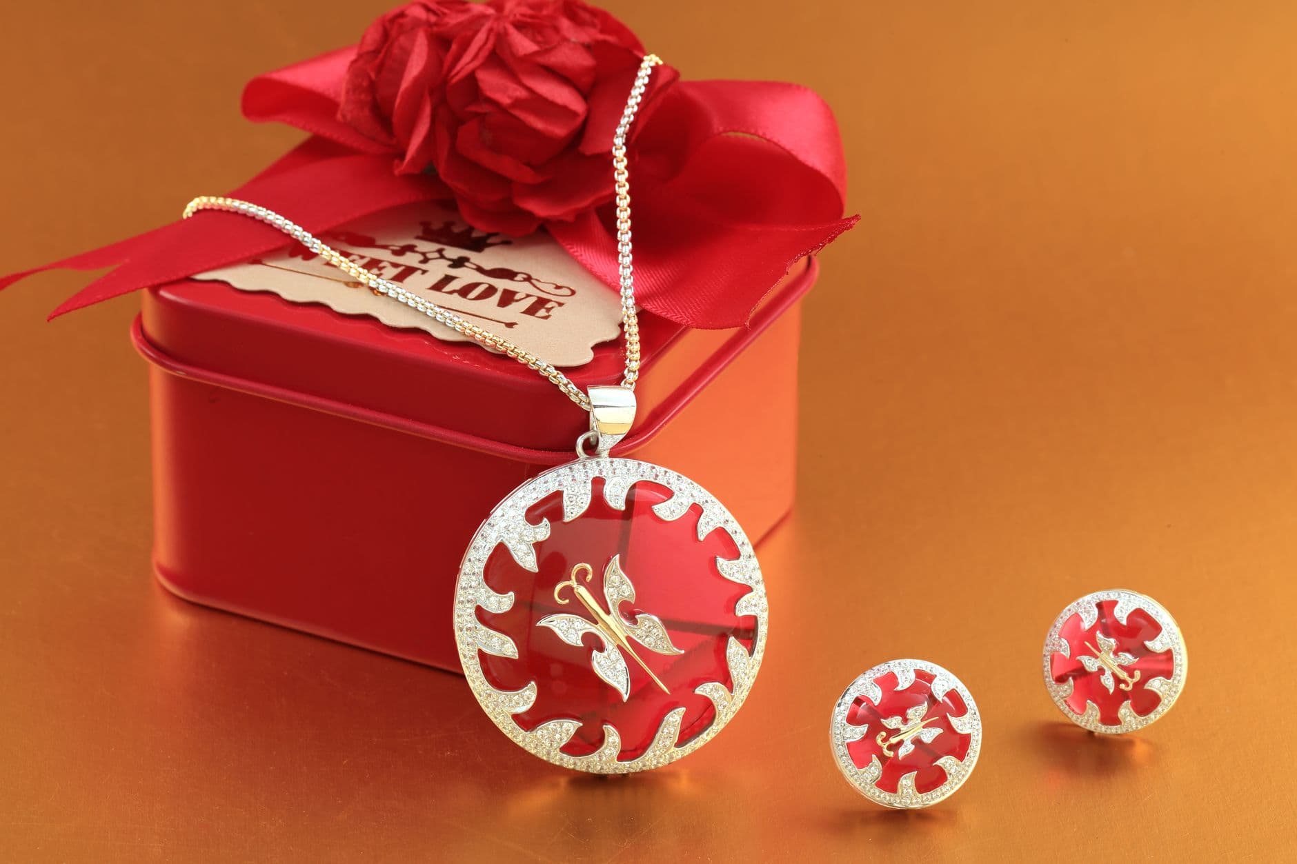 Silver jewelry set with red accents beside a decorative gift box.