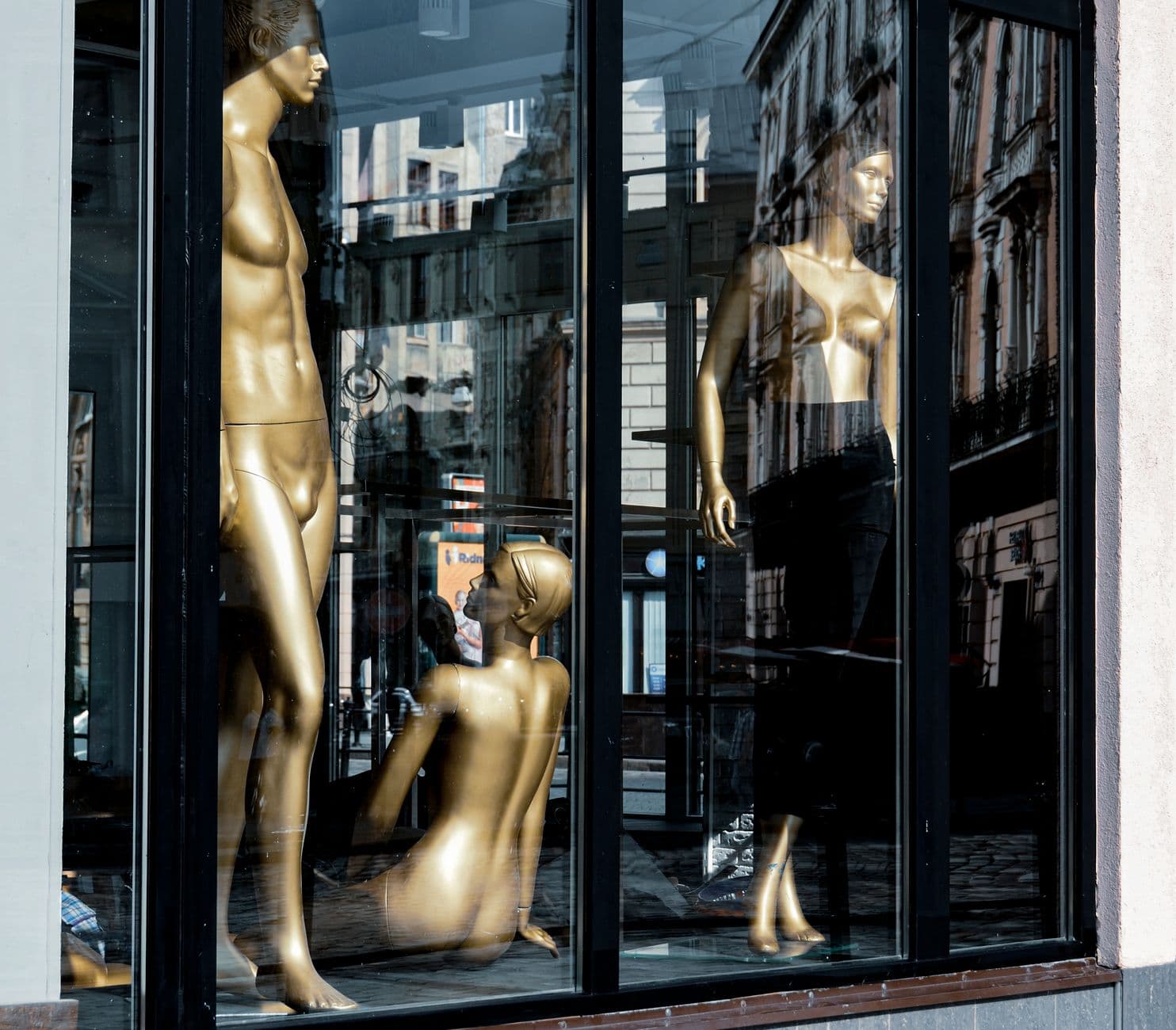 Golden mannequins displayed in a Lviv store window reflecting urban architecture.