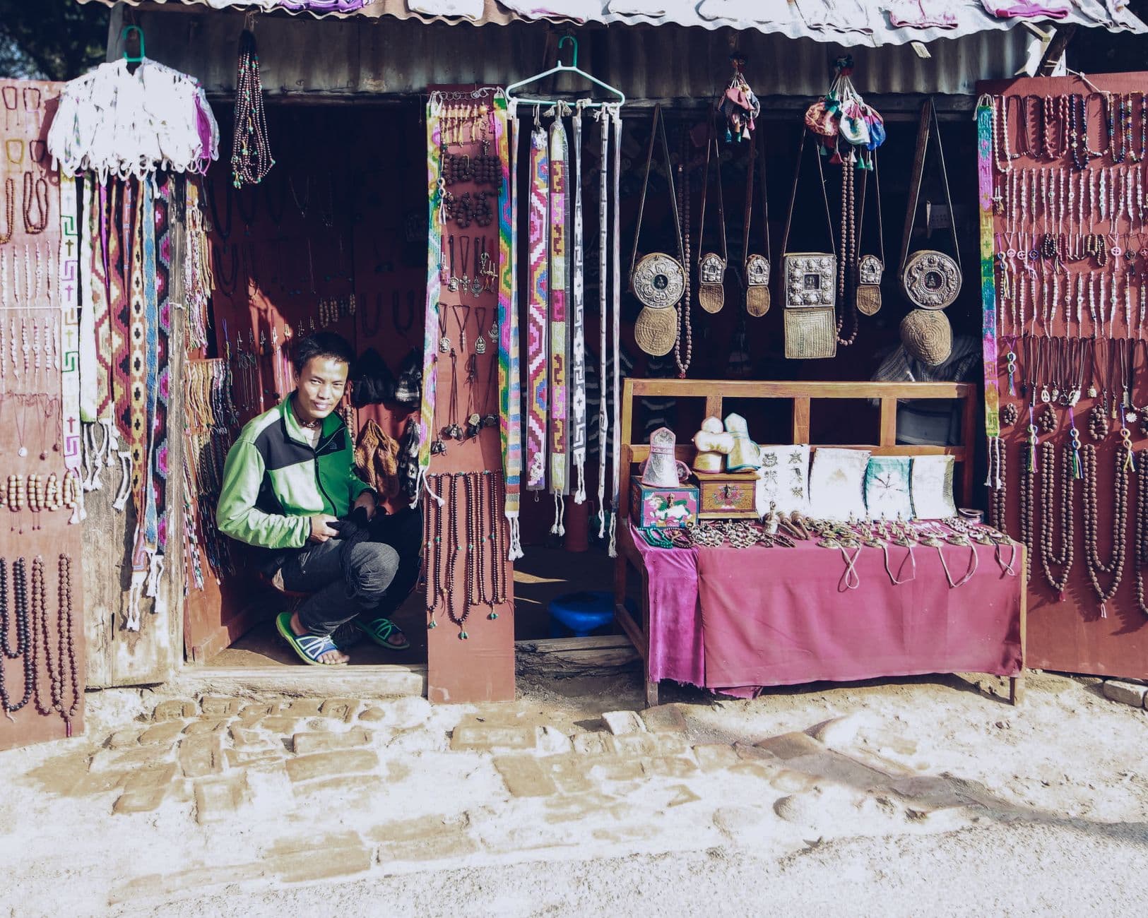 A man crouches in a vibrant retail shop selling handmade jewelry and decorative crafts.