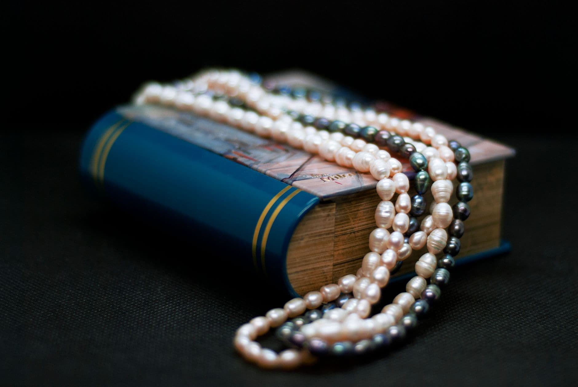 A close-up of elegant pearl necklaces draped over a blue hardcover book.