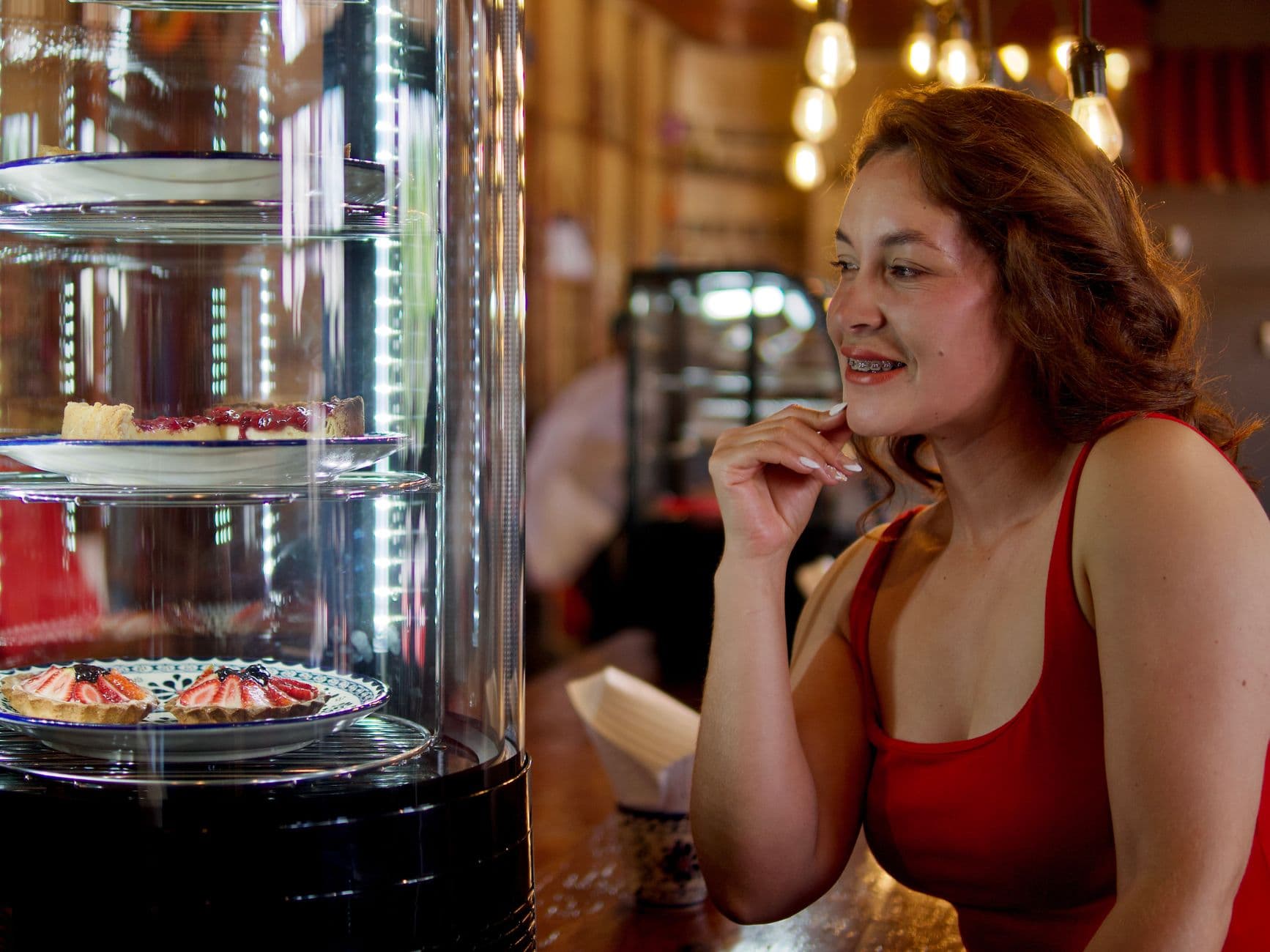 A woman in a café admires dessert display, creating a warm, inviting atmosphere.