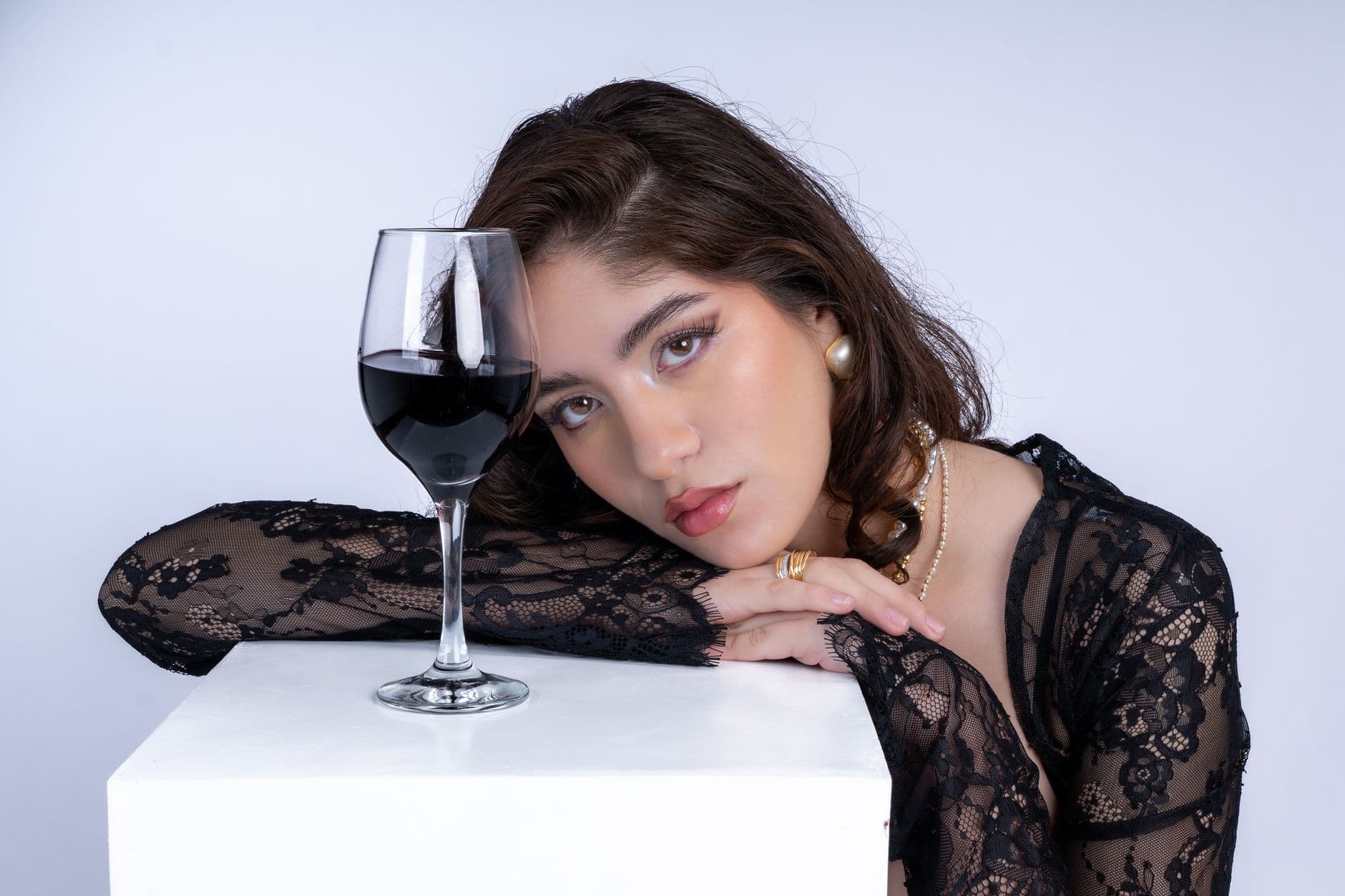 A fashion-forward woman posed elegantly with a glass of red wine in a studio setting.
