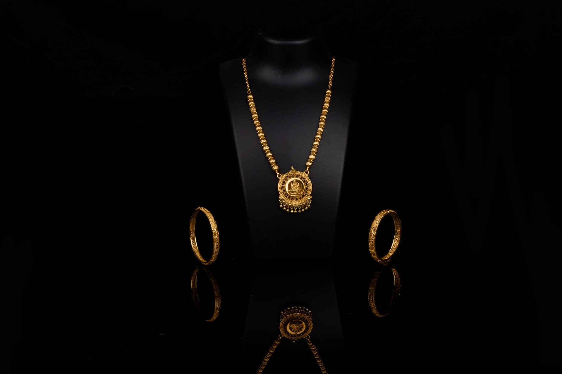 Luxurious gold necklace and bangles elegantly displayed against a dark backdrop, reflecting opulence.
