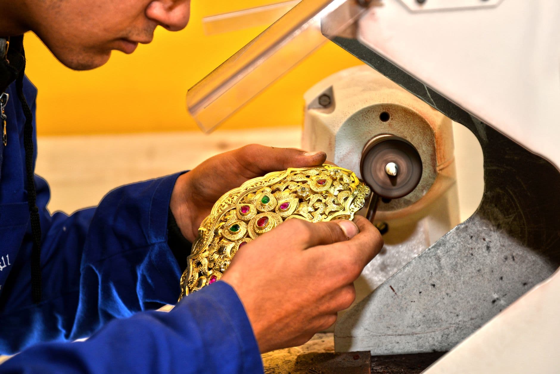 Skilled artisan polishing intricate gold jewelry piece using machinery in a Fès workshop.