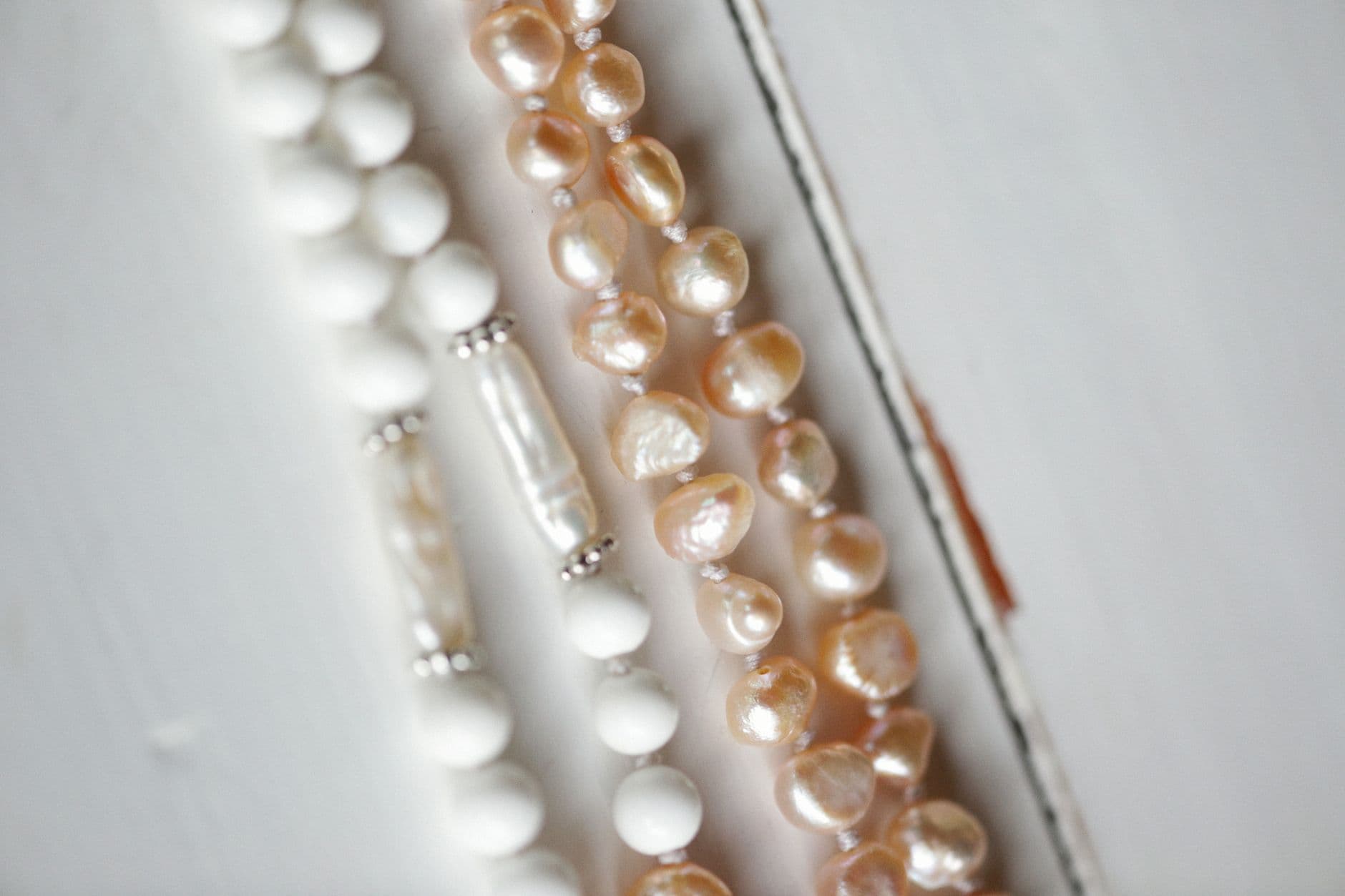 Close-up of elegant pearl and bead necklaces displayed on a white surface, showcasing delicate jewelry design.