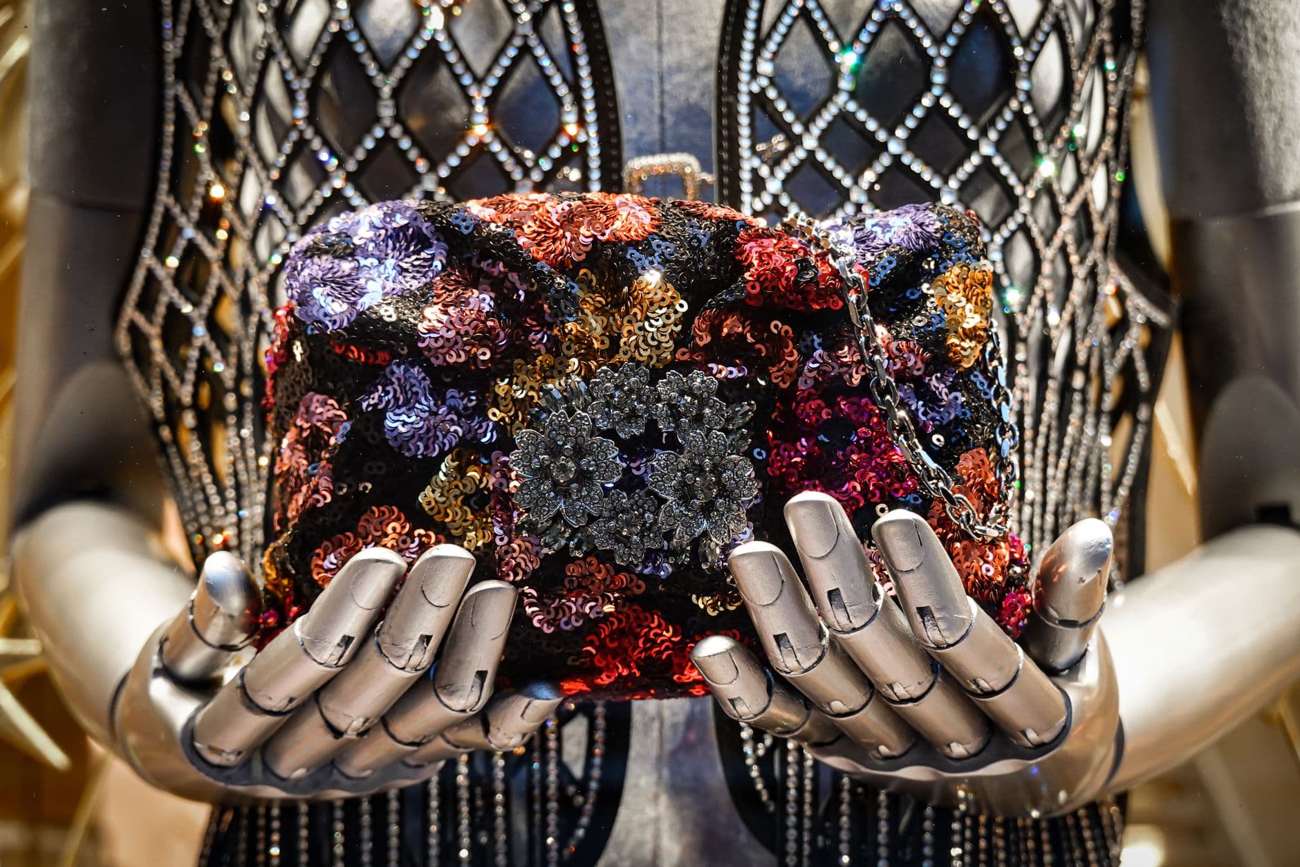 A fashion mannequin showcases a colorful sequin handbag held gracefully by robotic hands.