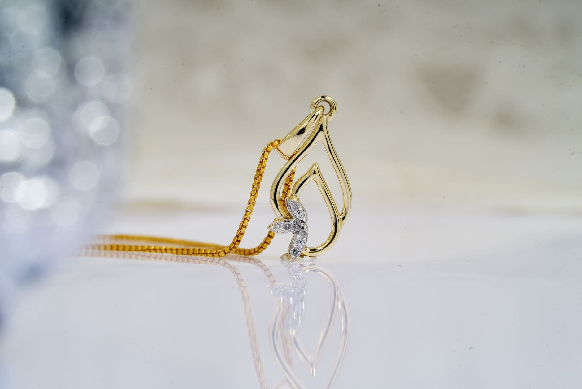 Small precious diamonds in golden shiny pendant on necklace placed on reflective white surface of table