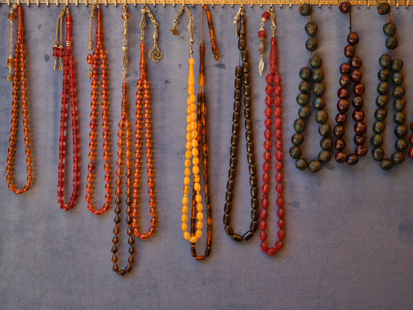 Collection of vibrant beaded necklaces hanging neatly on a gray wall.