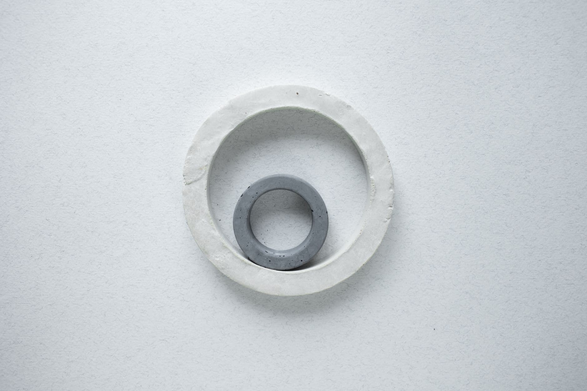 Minimalist photograph of two ceramic rings forming a circular pattern on a white textured background.